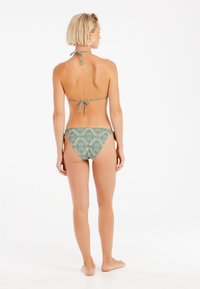 Bikini dwuczęściowy w zielonym materiale z geometrycznym wzorem. Zawiązywany na szyi i po bokach, charakteryzujący się minimalnym zakryciem i gładką fakturą.