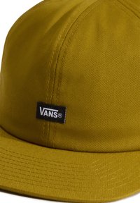 Gul texturerad tygkeps med platt skärm, försedd med en svart rektangulär etikett som visar "VANS" i vit text.
