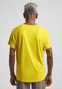 T-shirt atletico giallo realizzato in tessuto testurizzato, con scollatura a girocollo e maniche corte, visto da dietro.