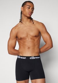 Schwarze Boxershorts mit einem weißen "ellesse"-Logo am elastischen Bund. Der Stoff wirkt glatt und dehnbar, entworfen für Komfort und Passform.