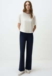 Witte, kortemouwtop gecombineerd met marineblauwe, flared broek en witte sneakers. Gladde stof en een relaxed fit in de hele outfit.