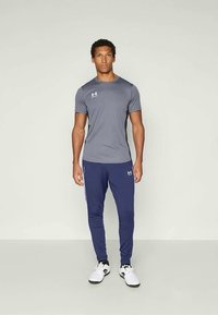 Szürke, nedvességelvezető sportpóló rövid ujjakkal, amelyet sötétkék, slim-fit jogger nadrággal párosítanak, fehér oldalsávokkal és logóval.