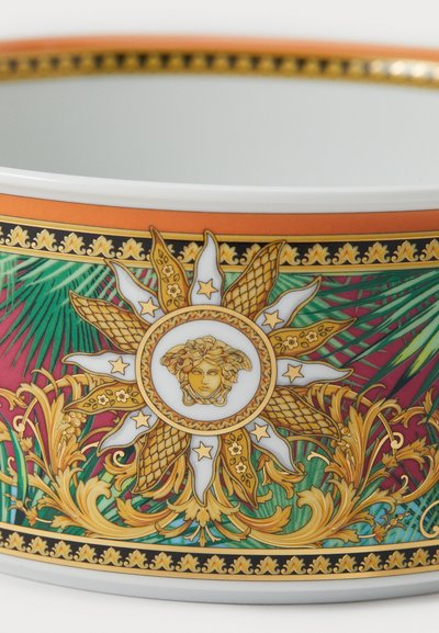Porculanska zdjela s živopisnim uzorkom koji uključuje zlatne naglaske, glavu Meduze, sunčev zrak i tropske listove u zelenoj, ružičastoj i narančastoj boji.