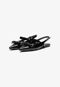 Čierne kožené slingback topánky s špicatými špičkami, obsahujúce dva detaily s mašľou a nastaviteľné remienky okolo členkov. Ploché podpätky a hladká textura.