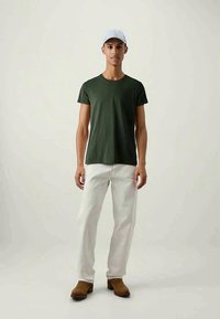 T-shirt verde a maniche corte abbinato a pantaloni bianchi e calzature marroni; design semplice, vestibilità comoda e texture morbida. Cappellino azzurro.