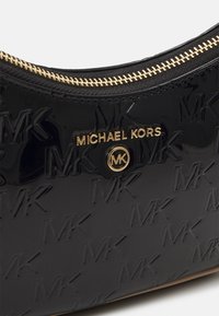 Svart patenterad läderhandväska med präglad "MK"-logotyp, guldfärgad hårdvara och en dragkedja längs toppen. Slät textur.