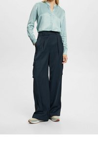 Ljusblå blus med V-ringning och långa ärmar, ihopparad med marinblå vida cargobyxor med sidofickor. Skorna visar lager av pastellfärger.