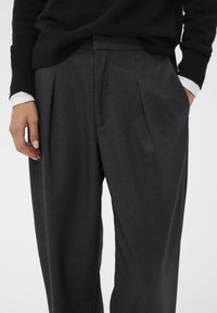 Grijze op maat gemaakte broek van geweven stof, met plooien, een relaxte pasvorm en zijzakken. Gestyled met een zwarte sweater.