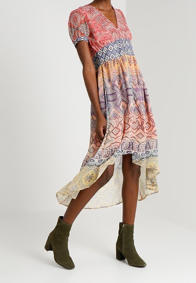 Robe midi multicolore avec un col en V, des manches courtes bouffantes et des motifs tourbillonnants. Des bottines vert foncé aux chevilles complètent la tenue.