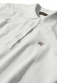 White polo shirt with a ribbed texture, featuring a collar, three white buttons, and an embroidered "HEY ammo" logo in brown.