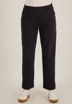 Zwarte rechte broek met details aan de voornaad, gedragen met witte sneakers met rubberen zolen.