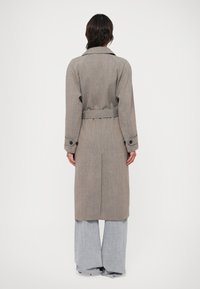 Szary w kratę długi płaszcz z paskiem, kołnierzem i mankietami na guziki. Ma prosty krój i rozcięcie z tyłu, w połączeniu z jasnoszarymi szerokimi spodniami.