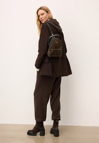 Pruun üleüldine mantel kapuutsiga, sobivad laiad pruunid püksid ja pruunid kontsakingad. Väike leopardimustriga seljakott kuldsete detailidega.