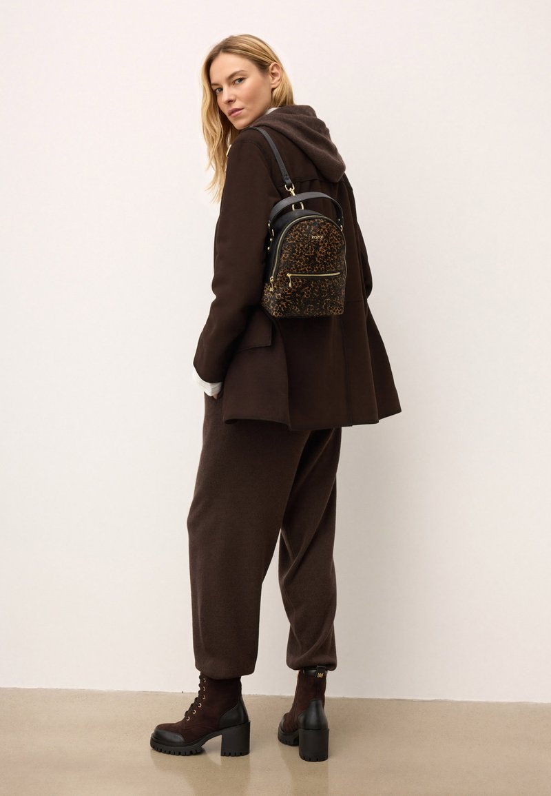 Pruun üleüldine mantel kapuutsiga, sobivad laiad pruunid püksid ja pruunid kontsakingad. Väike leopardimustriga seljakott kuldsete detailidega.