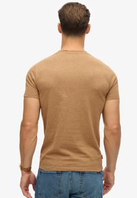 Maglietta marrone a maniche corte con colletto rotondo, realizzata in tessuto morbido. Presenta una vestibilità aderente e dettagli decorativi minimi sul retro.