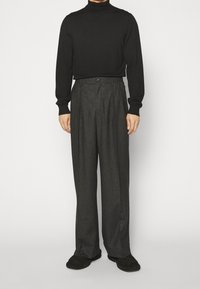 Czarny golf o dopasowanym kroju, zestawiony z wysokim stanem szarymi plisowanymi spodniami. Miękka faktura, szerokie nogawki, minimalne zdobienia.