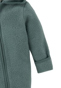 Groene fleecejack met een zachte textuur, voorzien van een ritsluiting en een capuchon. De mouwen zijn elastisch, wat zorgt voor een snug fit.