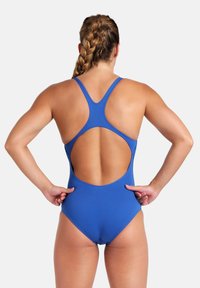 Blå badedragt i ét stykke med racerback-design, åben ryg og glat tekstur; har strækbart stof og minimal sømdetaljering.