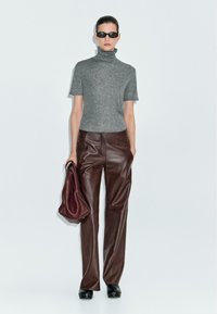 Maglione a collo alto grigio a maniche corte, pantaloni in pelle marrone, occhiali da sole neri e una borsa bordeaux; texture lisce e design aderente.