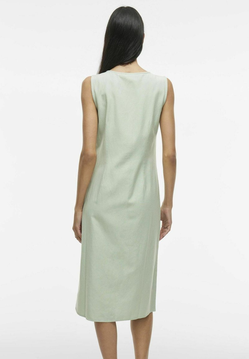 Robe sans manches vert clair avec un corsage ajusté et une jupe évasée arrivant au genou. Texture lisse, design minimaliste, sans motifs visibles.