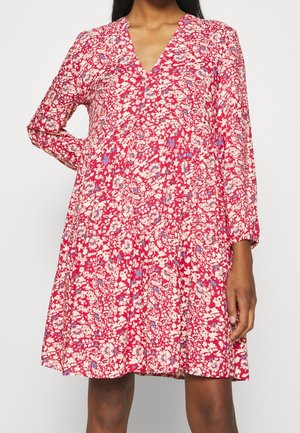 Rosa blommig klänning med lång ärm, V-ringning, avslappnad passform och lager-på-lager kjol med olika vita och blå blommönster.