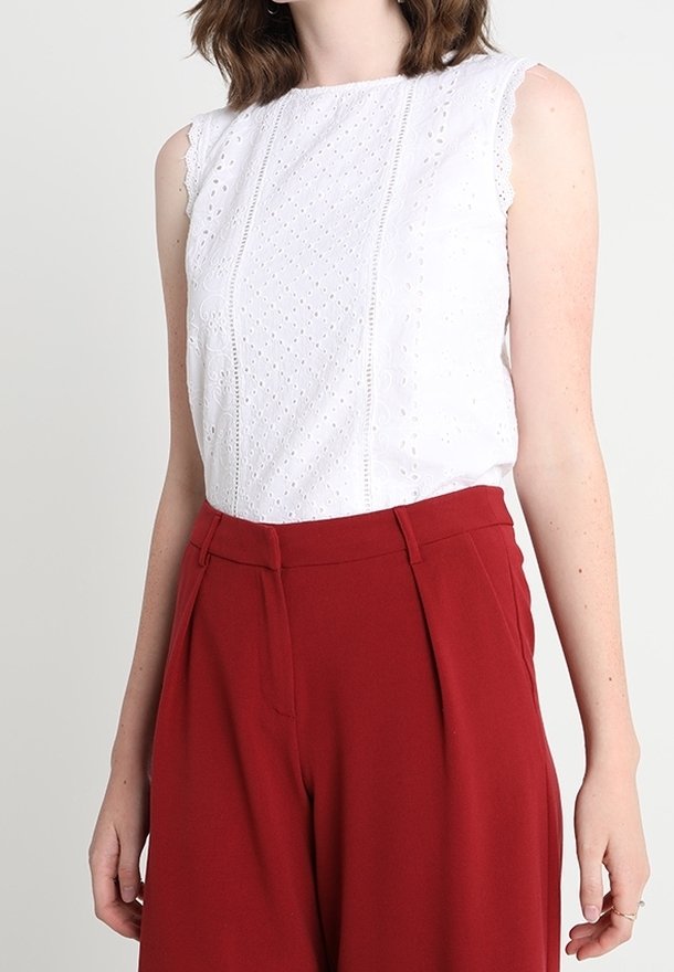 Bílý bezramínkový top s vyšívanými detaily, s vroubkovanými okraji; spárován s vysokým pasem a širokými červenými kalhotami s přehyby v přední části.