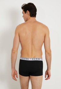 Čierne boxerky s bielym pásom so svojim logom "GUESS". Hladká textúra, priliehavý strih a dĺžka do polovice stehna.