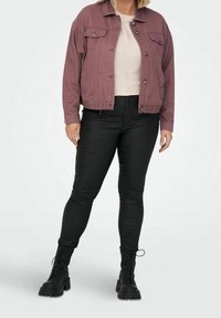 Chaqueta de mezclilla color rosa con cierre de botones, dos bolsillos en el pecho, combinada con pantalones pitillo negros y botas negras con cordones.
