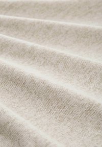 Tessuto beige chiaro con una superficie morbida e texturizzata. Presenta sottili variazioni di colore e modello, evidenziando un design piegato.