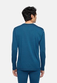 Langärmliges blaues Shirt aus weichem Stoff, mit Rundhalsausschnitt und kontrastierenden Steppnähten entlang der Kanten und Ärmel.