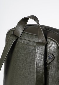 Groene leren rugzak close-up, met een gestructureerde afwerking, dubbele handvatten, stikseldetails en ritsbeslag.