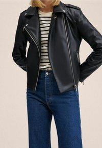 Veste biker en similicuir noir avec une coupe ajustée, une fermeture éclair asymétrique et des garnitures argentées, portée avec un t-shirt rayé et un jean bleu.