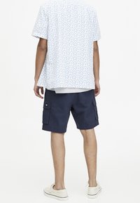 Kortærmet hvid skjorte med blåt mønster, parret med marineblå cargo shorts med to sidelommer. Båret med lyse sneakers.