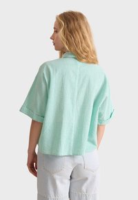 Green and white striped short-sleeve shirt, collared, with a textured fabric; worn with light blue, loose-fitting shorts.
