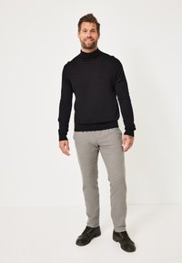 Schwarzer Rollkragenpullover, graue maßgeschneiderte Hose und schwarze Schnürschuhe. Das Outfit zeichnet sich durch eine figurnahe Passform und glatte Texturen aus.