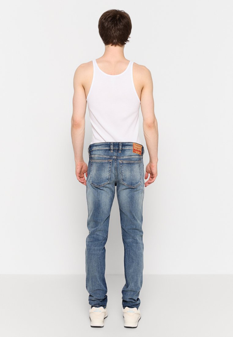 Jeans in denim blu sbiadito con taglio dritto, cinque tasche e un'etichetta in pelle marrone sulla cintura posteriore. Canottiera bianca indossata sotto.