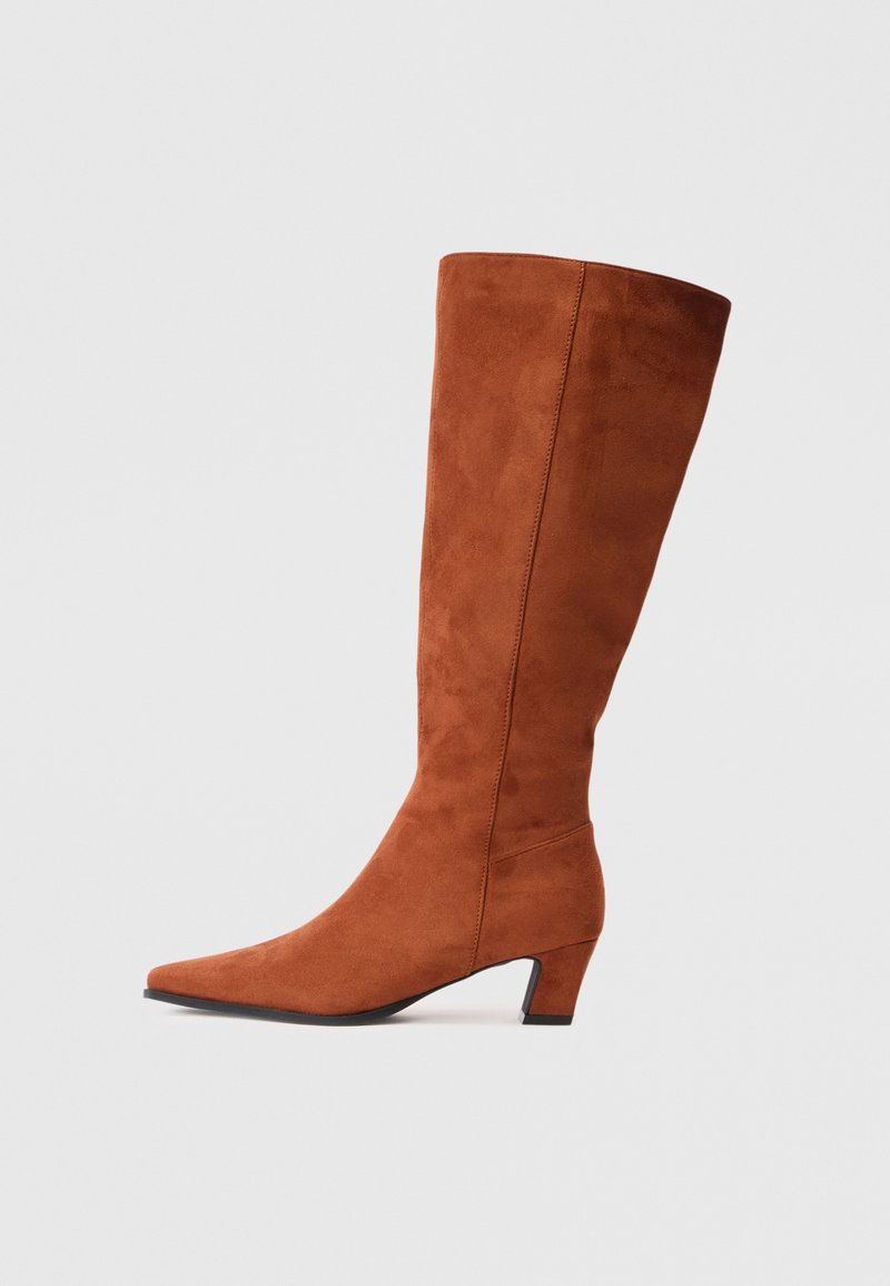 Stivale marrone in suede alto fino al ginocchio con punta affusolata e tacco a blocco piccolo, caratterizzato da una superficie liscia e un design minimalista.