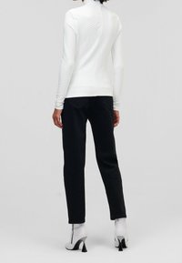 Biała bluzka z długim rękawem z teksturowanym wzorem w romby, w zestawieniu z czarnymi spodniami i białymi botkami za kostkę z metalicznym obcasem.