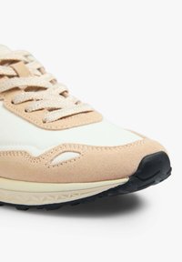 Hellbeige und weiße Sneaker aus Wildleder und Leder mit gepolsterter Zunge, runder Zehenpartie, strukturiertem Profil und kontrastierenden schwarzen Gummi-Accents.