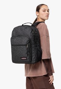 Svart och vit rutig ryggsäck med flera fickor med dragkedja, övre handtag och justerbara remmar. Hållbart material med texturerad yta.