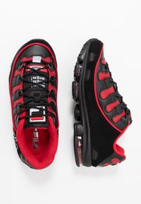 Chaussures de sport noires et rouges avec tige en maille et synthétique, languette rembourrée, semelle en caoutchouc et unité air visible dans le talon.