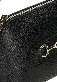 Černá kožená kabelka s texturovaným povrchem, zlatým zipem a stříbrným kováním. Obsahuje dekorativní řetězovou linku.