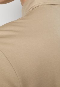 Close-up of beige fabric shirt focusing on the shoulder and collar area with visible stitching details.