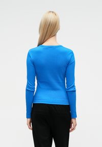 Pitkähihainen, istuva paita kirkkaan sinisestä resorikankaasta, pyöreällä pääntiellä, yhdistetty mustiin, väljälahkeisiin housuihin.