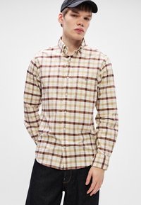 Camicia button-up beige con motivo a quadri marrone e crema. Caratterizzata da maniche lunghe, colletto e una piccola tasca sul petto.