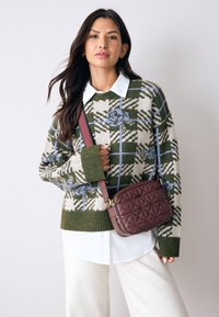 Strikket trøje med ternet mønster i grønt, creme og blåt; hvid skjorte under; brun quiltet crossbody-taske; model i lyse beige bukser.