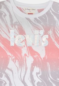 T-shirt branca com um padrão mármore em rosa e cinza, com um destacado logotipo refletor "levi's" em destaque ao centro.