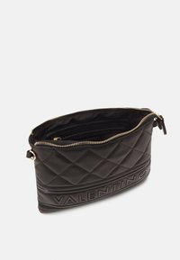 Crna torbica od quilted kože s zlatnim zatvaračem, koja na prednjoj strani ima urezani naziv brenda te obloženi unutarnji prostor s džepovima.