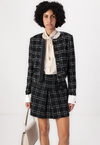 Tailored black and white plaid blazer with a matching skirt, made from textured fabric, featuring silver hardware and a beige blouse with a tie.