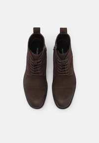Bottes marron en daim à la cheville avec une finition lisse, dotées de lacets et de fermetures éclair latérales, semelles en caoutchouc et détails de coutures contrastantes.